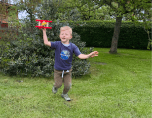 Junge läuft mit Doppeldecker in der Hand über eine Wiese